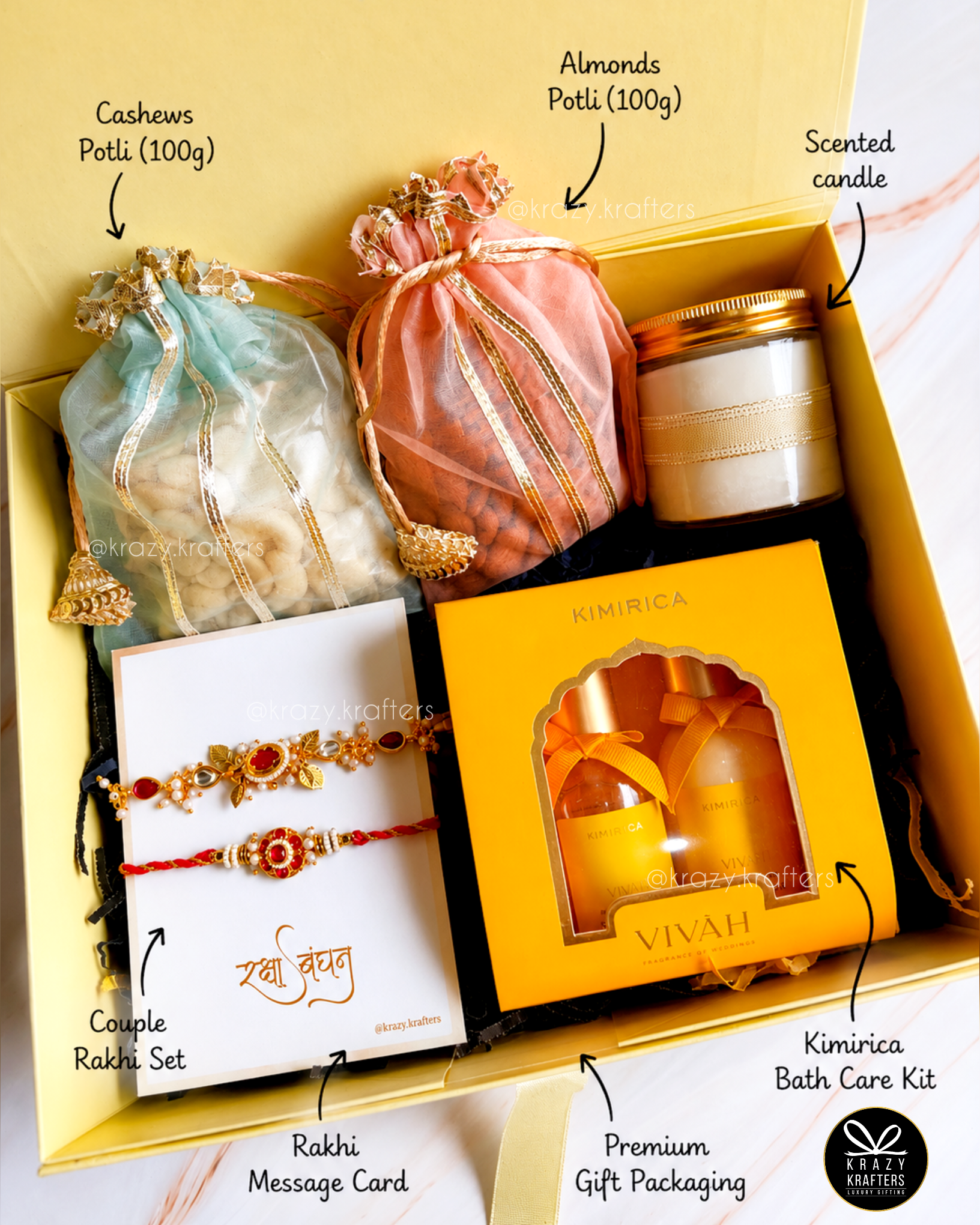 A curated gift box set labeled with callouts for each included item: a light blue drawstring pouch of cashews, a peach drawstring pouch of almonds, a scented candle, a Rakhi set on a white card, a message card, and a kimurica bath care kit in a yellow box. The set is arranged inside a yellow gift box with decorative ribbon and tissue paper.